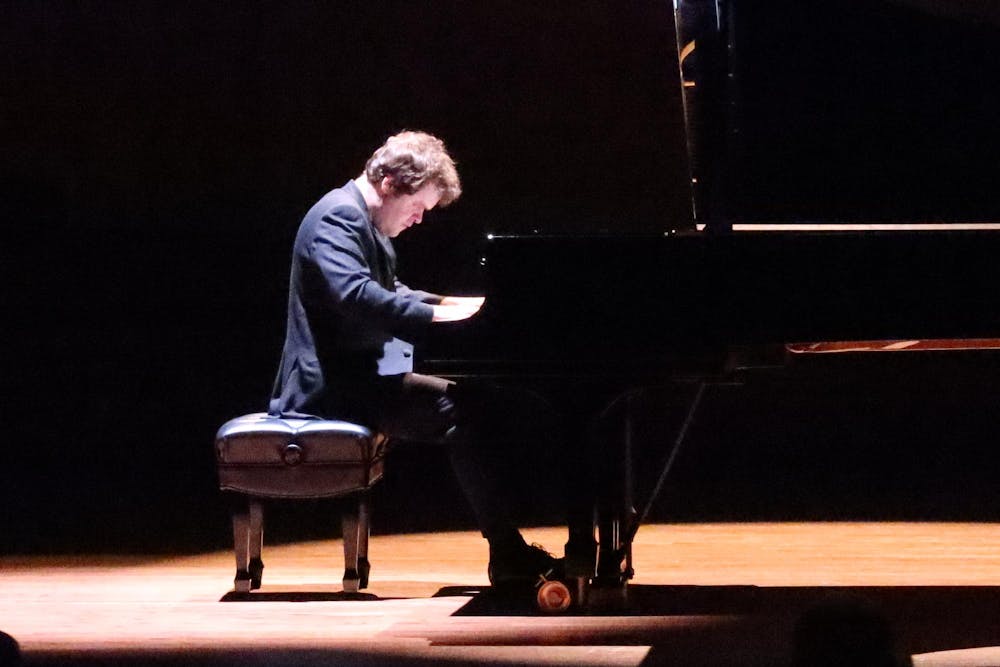 Man in tuxedo performs on a grand piano on stage. 