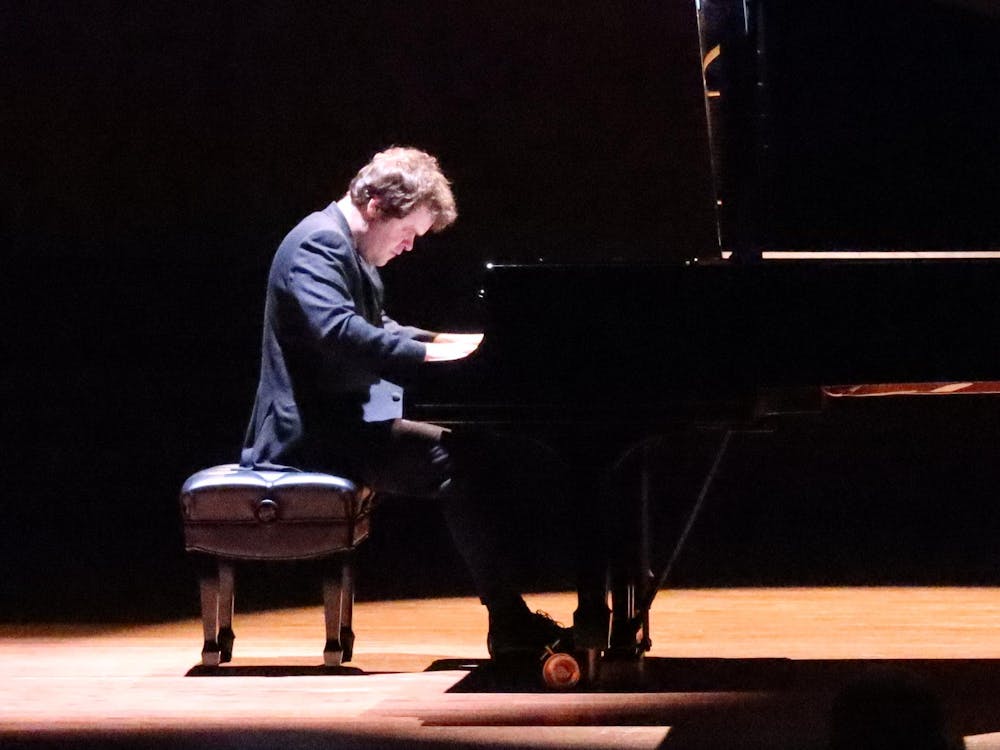 Man in tuxedo performs on a grand piano on stage.