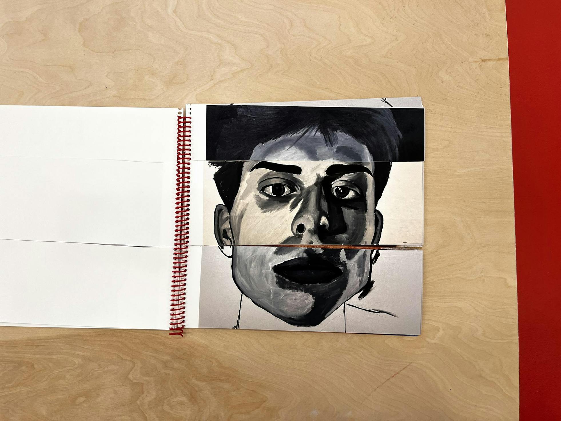 On a wooden table, a book with pages cut into three strips sits, open to an arrangement of eyes, nose, and a mouth. 