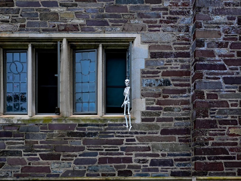 a skeleton hanging outside a window in a grey brick building with four visible windows