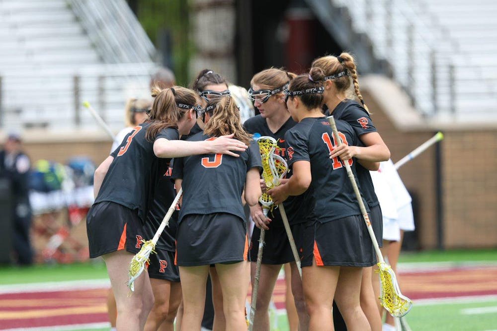 A group of women’s lacrosse players in black jerseys huddle around one another.