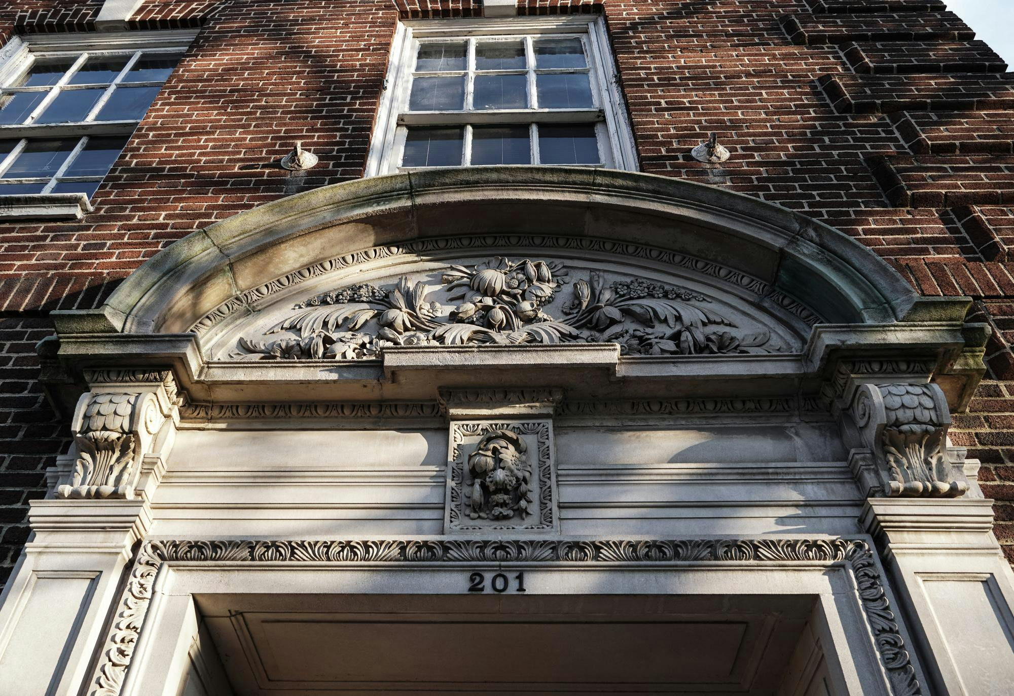 The sun sets over 201 Nassau Street a brown brick building with a gray stone gothic arch. The numbers "201" are above the door.