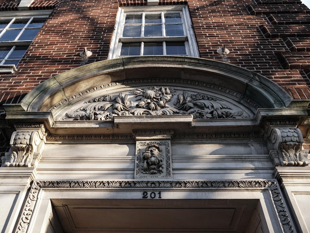 The sun sets over 201 Nassau Street a brown brick building with a gray stone gothic arch. The numbers "201" are above the door.