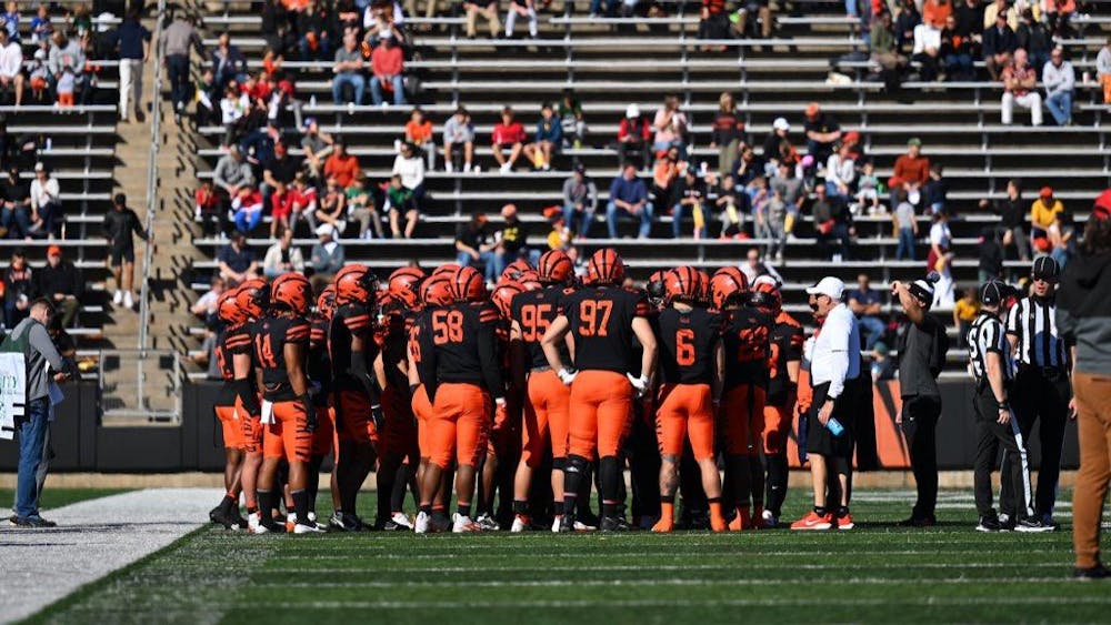 The backs of football players in orange and black uniforms, huddled on a field.