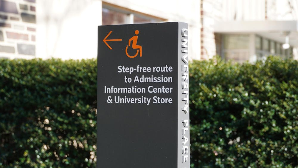 A gray sign with an orange arrow and text reading, “Step-free route to Admission Information Center & University Store”