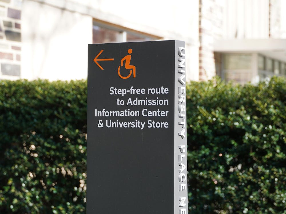 A gray sign with an orange arrow and text reading, “Step-free route to Admission Information Center & University Store”
