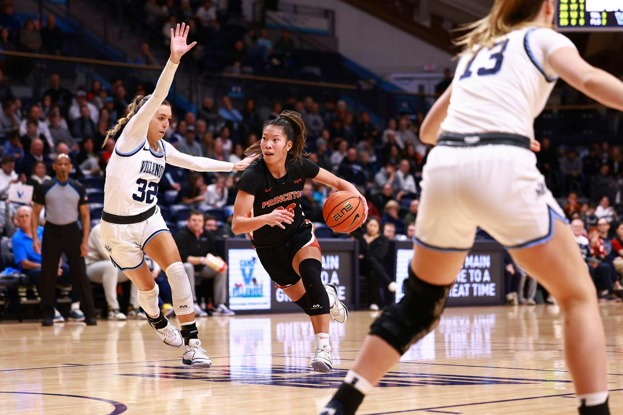 Player in orange and black dribbles basketball through two defenders in blue and white. 