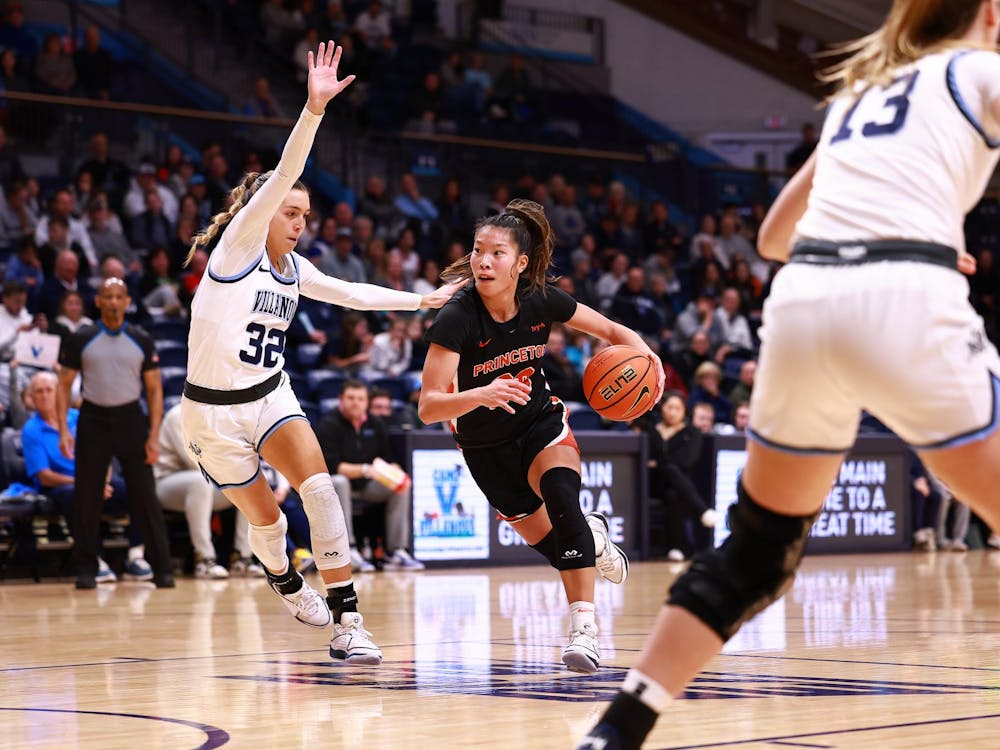 Player in orange and black dribbles basketball through two defenders in blue and white. 