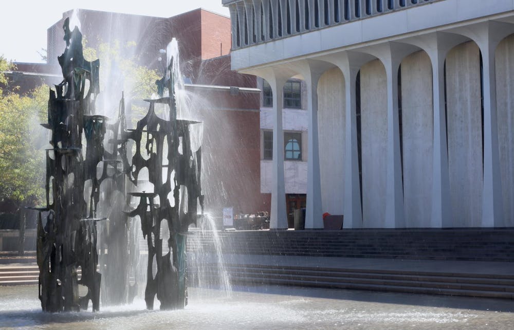 An abstractly-shaped fountain in front of a white building with large columns.