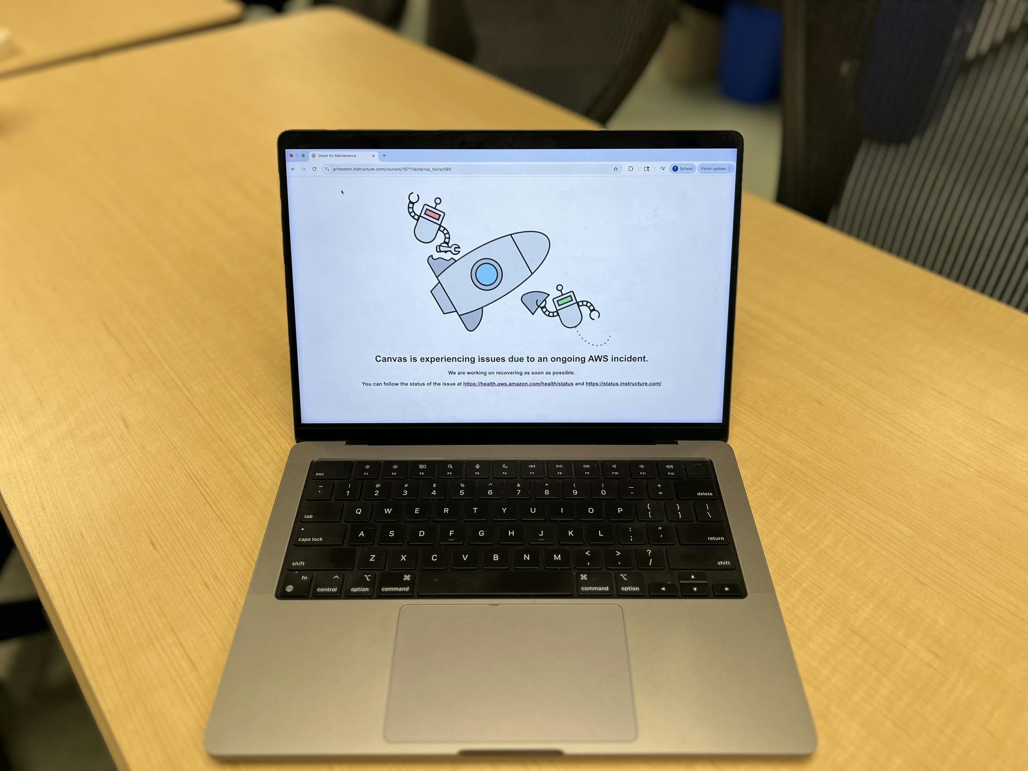 A silver computer on top of a wood table. The computer is a white screen with a rocket animation.