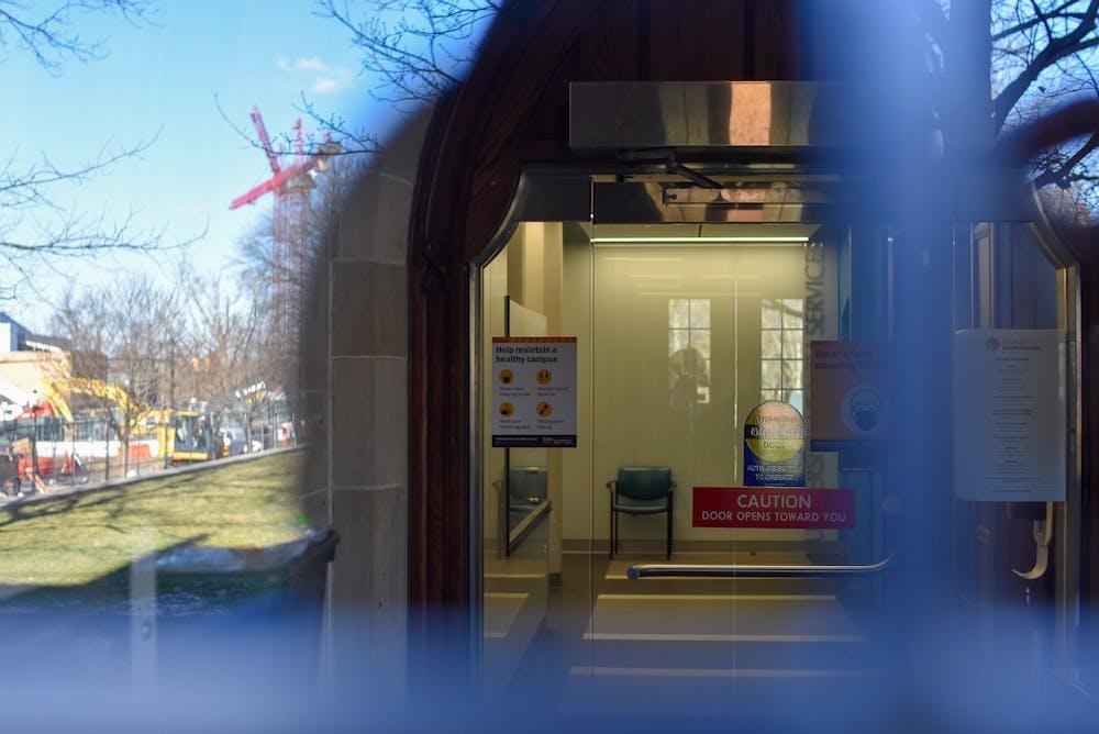 The entrance to Princeton's McCosh Health Center, with surrounding greenspace blurred and a focus on a yellow entryway through a glass door.