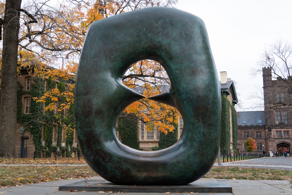 A green sculpture in the shape of an oval with points foregrounds fall foliage.