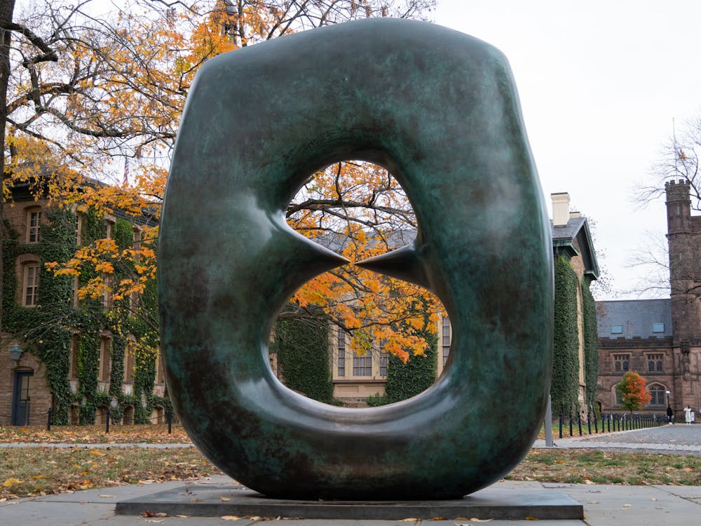 A green sculpture in the shape of an oval with points foregrounds fall foliage.