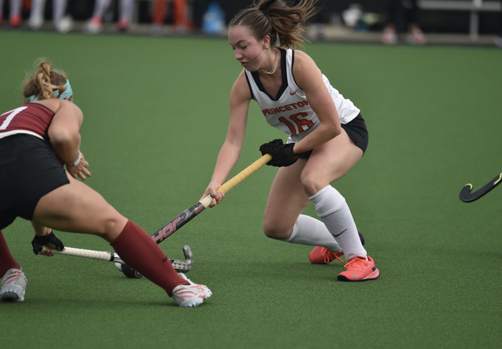 Field hockey girl in ponytail puts stick down to ground next to ball while opposing girl does the same