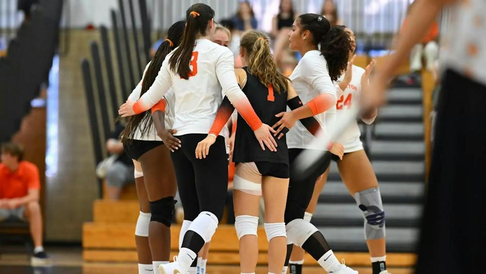 A group of volleyball players in a huddle wearing white and orange jerseys.