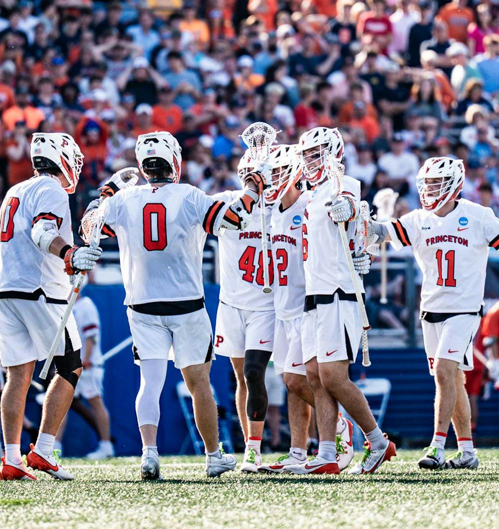 A group of Princeton Men's Lacrosse players in white and orange jerseys circling up together.