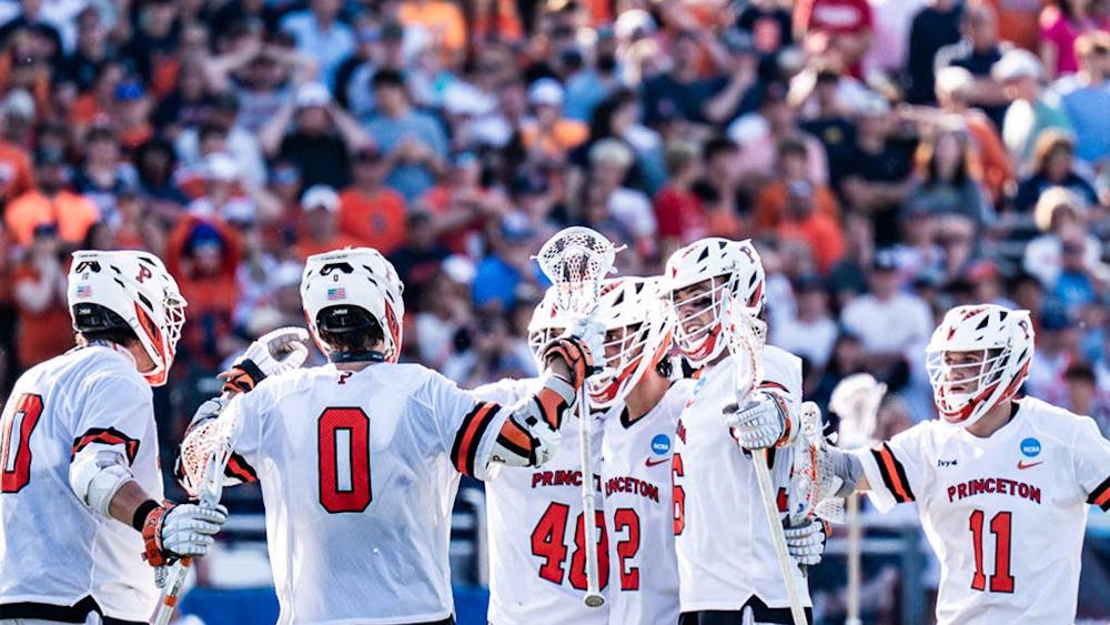 A group of Princeton Men's Lacrosse players in white and orange jerseys circling up together.