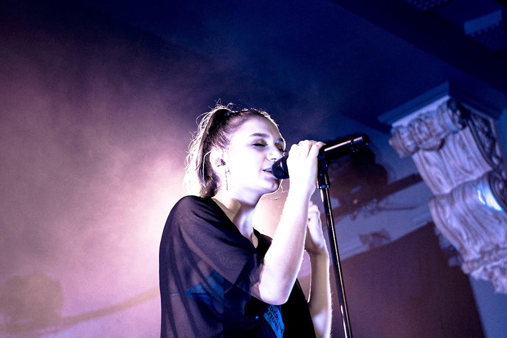 A woman singing into a microphone with purple lights shining in a halo behind her.