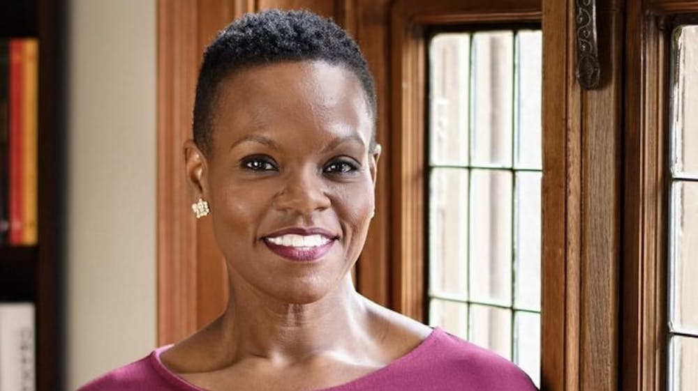 Theresa Thames smiles at the camera in the foreground, with a wooden wall and windows behind her.