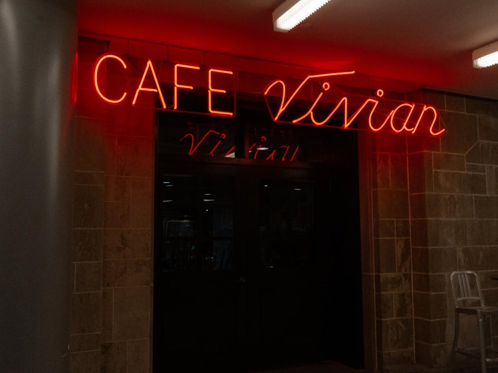A red neon sign reading "Cafe Vivian" sits in front of a concrete wall. 