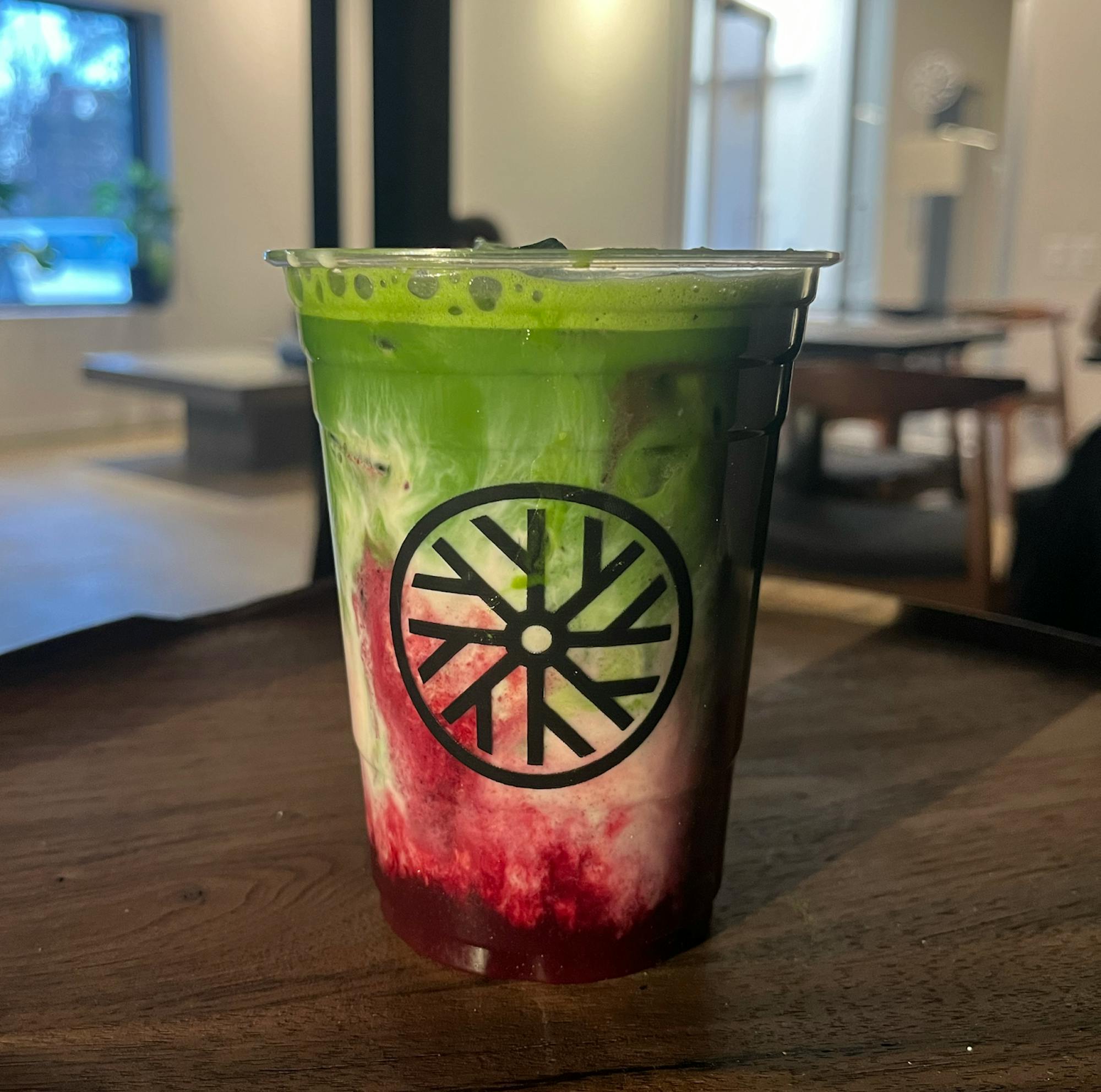 A cup of iced matcha, with the green matcha concentrated at the top of the cup and red cherry concentrated at the bottom. 