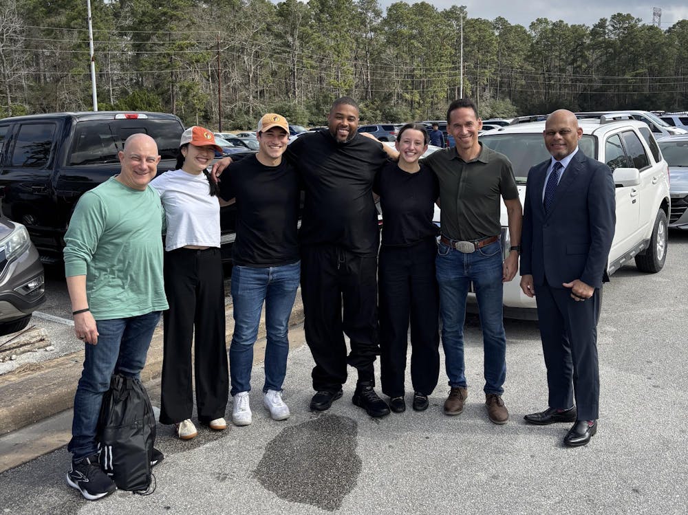 A group of seven people pose for a picture in a parking lot with trees in the background.