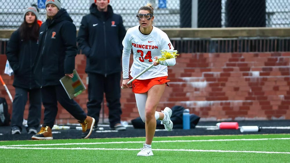 A woman on a grass field carrying a lacrosse stick.