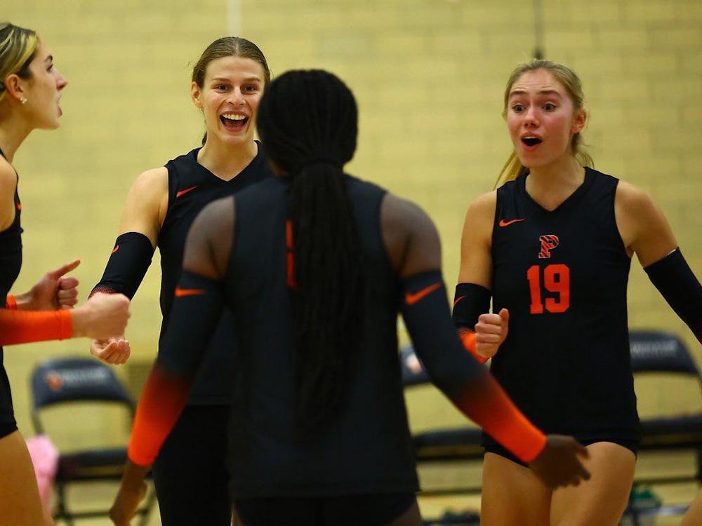 A group of women with volleyball uniforms on coming together on the court.
