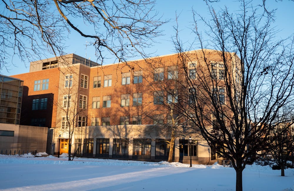 Sun shines on a brown brick building and trees on a snowy day. 