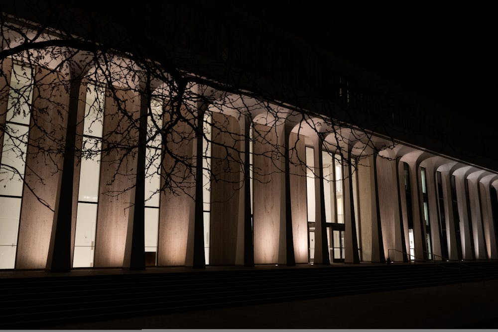 A white building with columns, surrounded by trees, is illuminated in the dark.