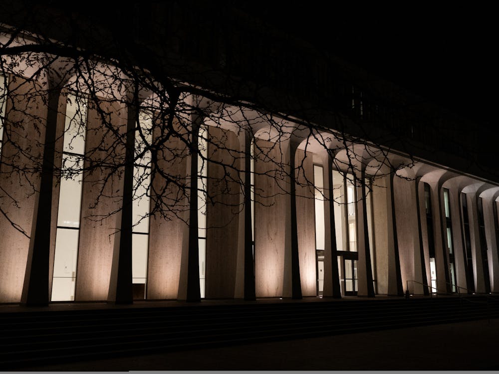 A white building with columns, surrounded by trees, is illuminated in the dark.
