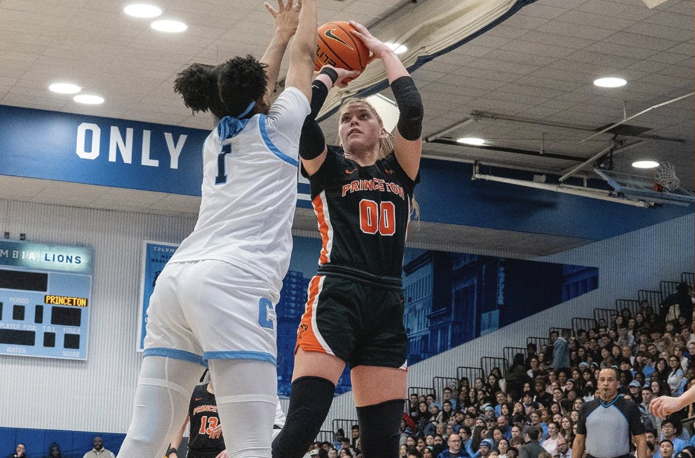 Women in black jersey shooting a basketball in crowded gymnasium.