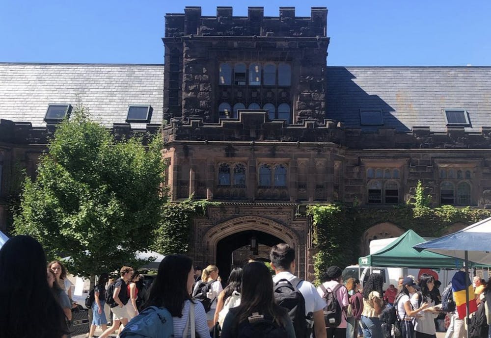 A crowd of people looking at vendors in front of an ivy-adorned building.