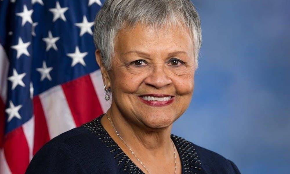 Un retrato de la representante estadounidense Bonnie Watson Coleman sonriendo frente a una bandera estadounidense y un fondo azul.