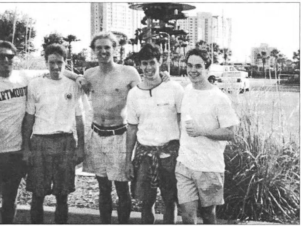 A black and white photograph of a line of 5 men smiling at the camera, wearing summer attire.