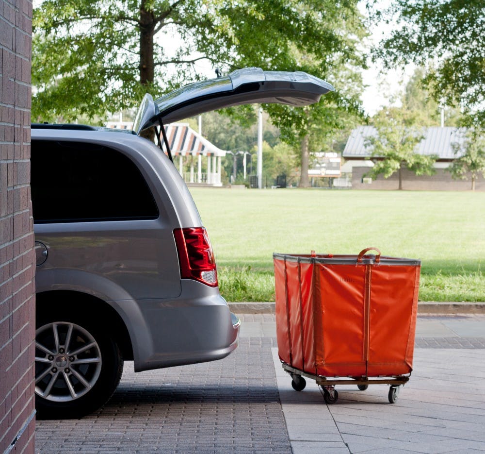 A grey SUV with the trunk open in front of an orange move-out cart.