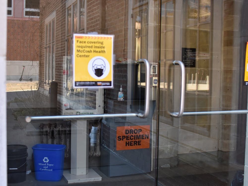 Glasss door with sign "Face covering required inside McCosh health center" with metal box with words "Drop Specimen Here" inside.