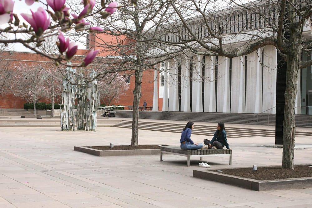 Two students talking on a bench outside the SPIA building in springtime. 