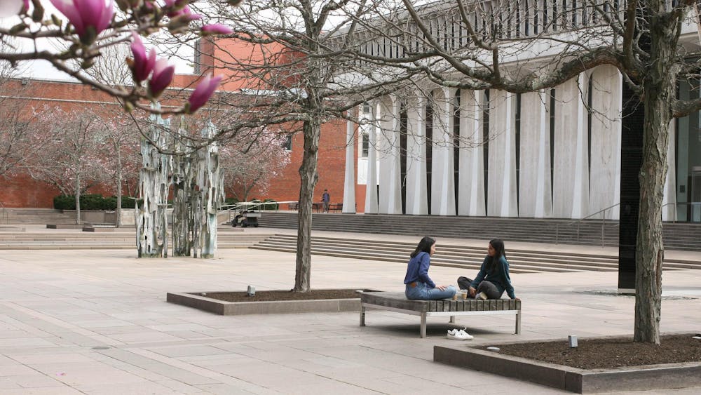 Two students talking on a bench outside the SPIA building in springtime.