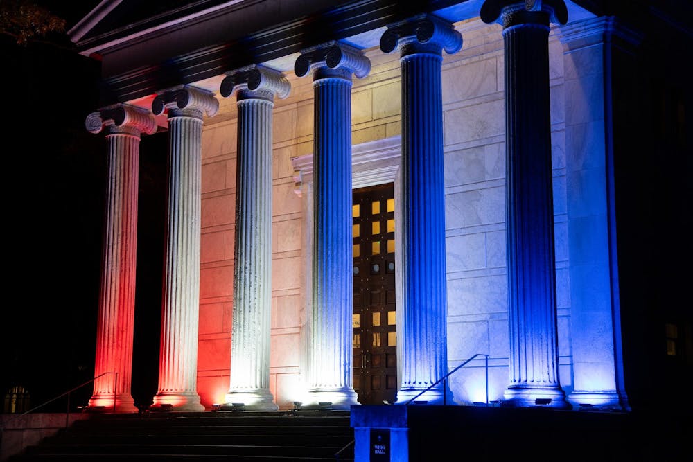 The front entrance of a building at night, illuminated with red, white, and blue lights.