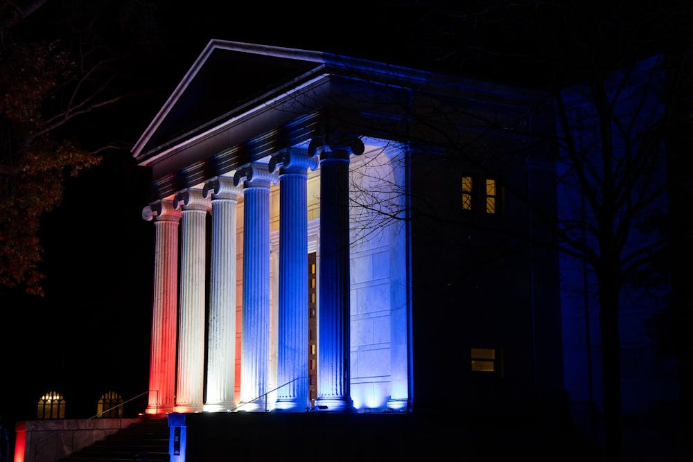 A large white building with columns is illuminated with red, white and blue lights.