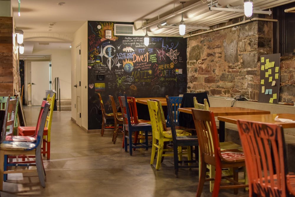 An empty cafe with colorful chairs, wood tables, a stone wall, and a chalkboard.