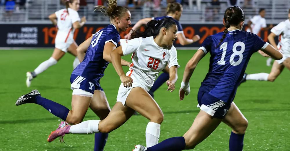 A woman in a white and orange jersey running towards the ball
