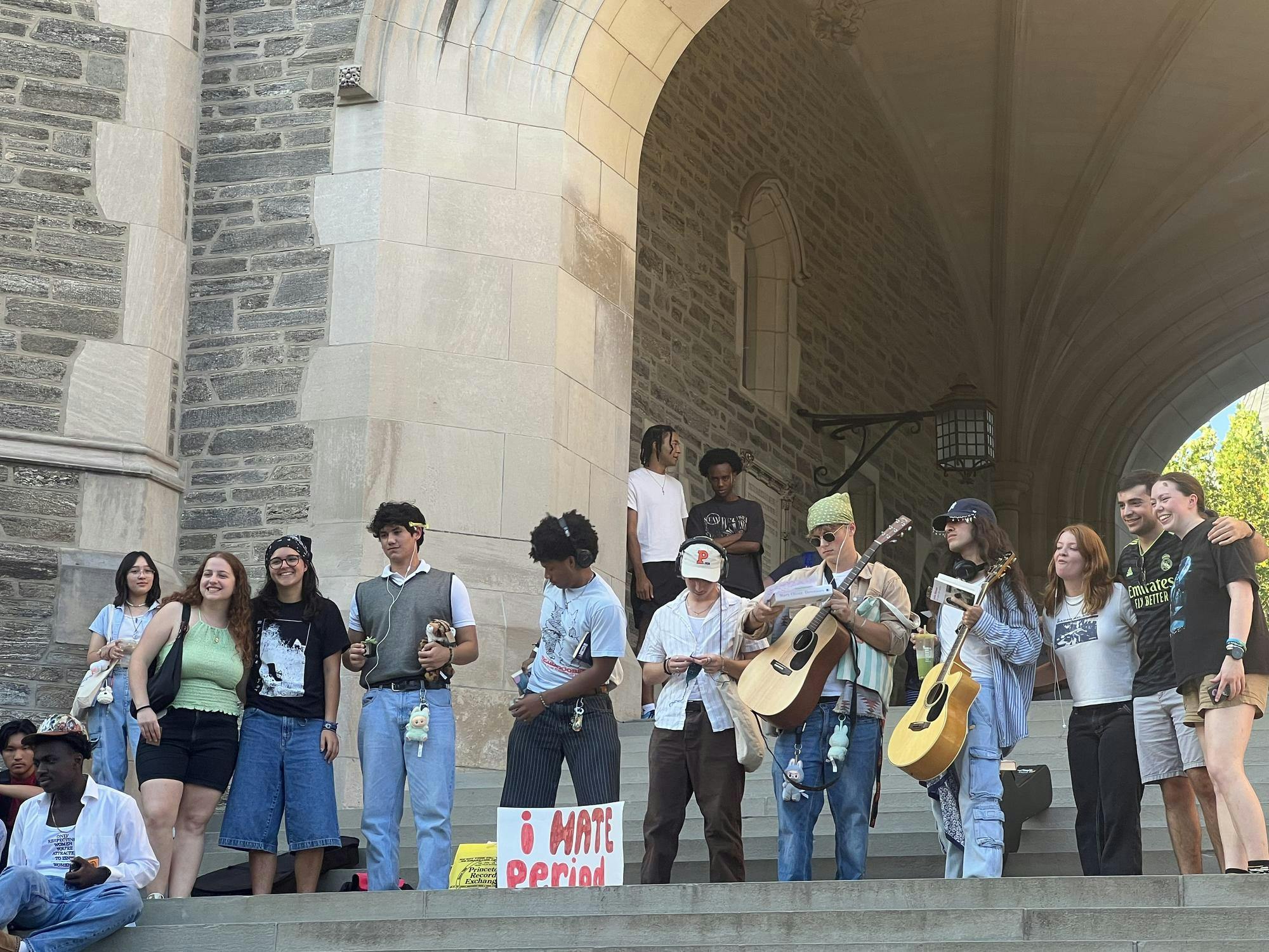 A group of people with Labubus, guitars, and other performative male style on the steps under an arch.