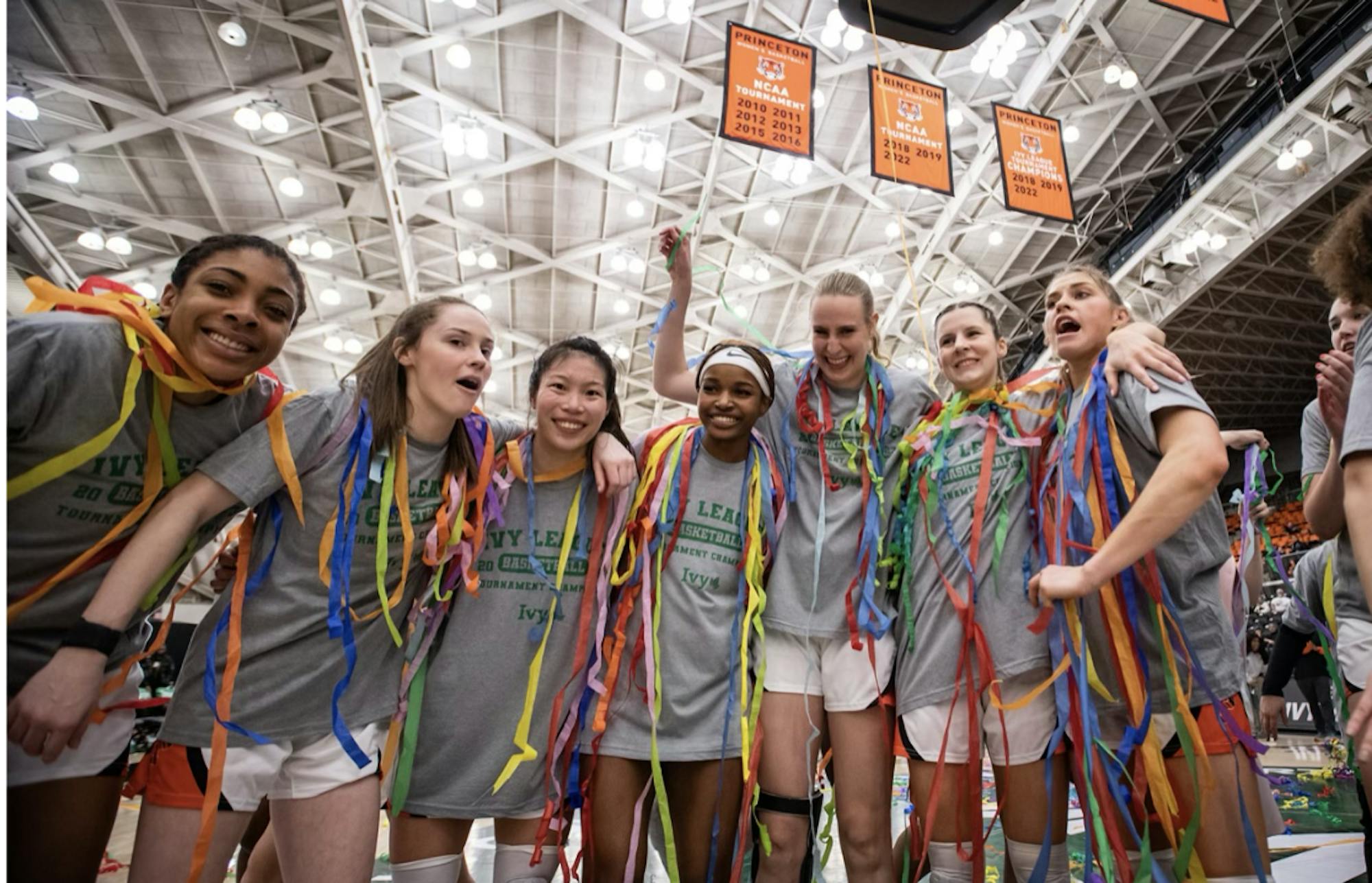 Women's basketball team huddled together celebrating win covered in streamers. 
