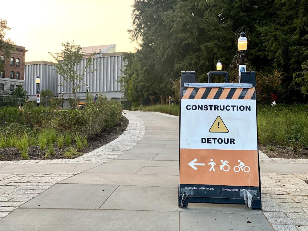 A picture of a detour sign in orange and black lettering standing in front of a gray sidewalk.