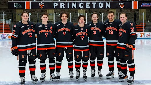 Seven hockey players in black and orange jerseys face the camera. 