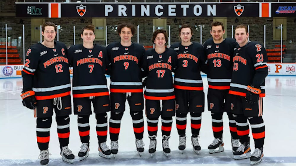 Seven hockey players in black and orange jerseys face the camera. 