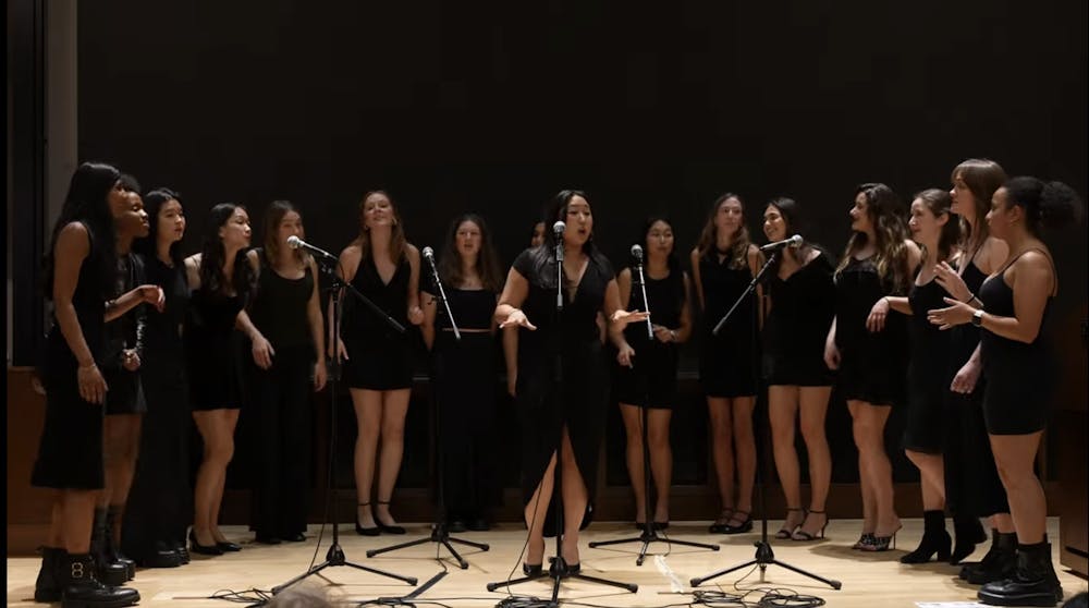 Women in black dresses singing on stage. One soloist stands in the middle.