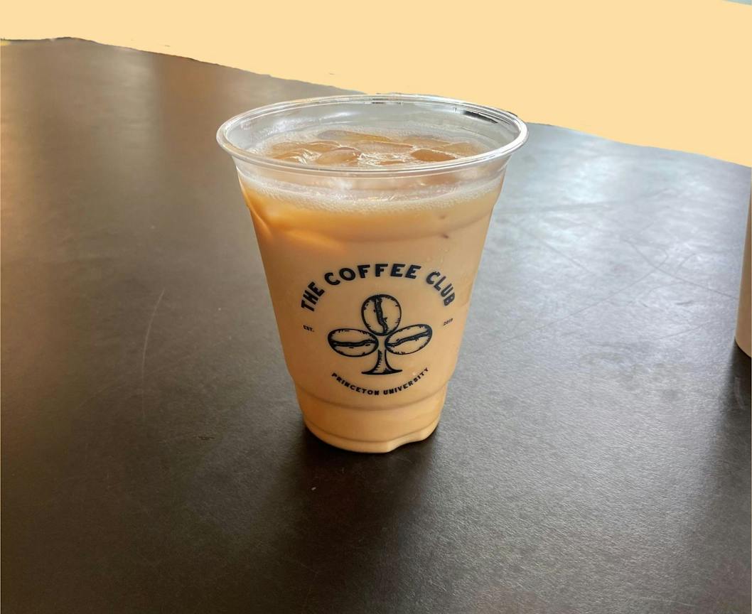 An iced blueberry pie latte sits on a table against a light orange background.